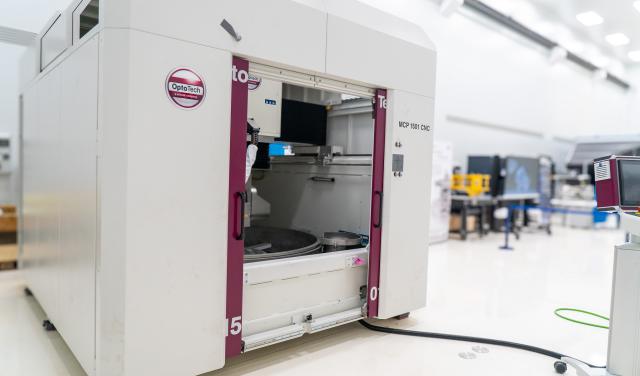A large white machine with two big doors (polishing machine for large surfaces) in a white room with high ceilings (IACTEC's south clean room).